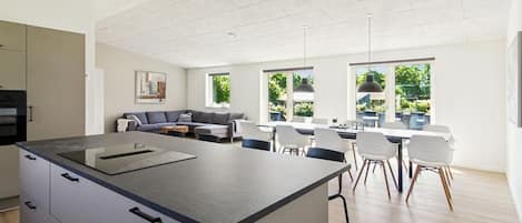 A modern kitchen with a central island, dining area with chairs, and a sofa.
