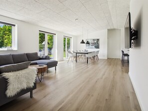 Una sala de estar moderna con un sofá, una mesa de comedor con sillas y un televisor montado en la pared.