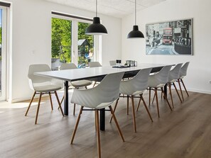 Een moderne eethoek met een lange tafel, witte stoelen en hanglampen.