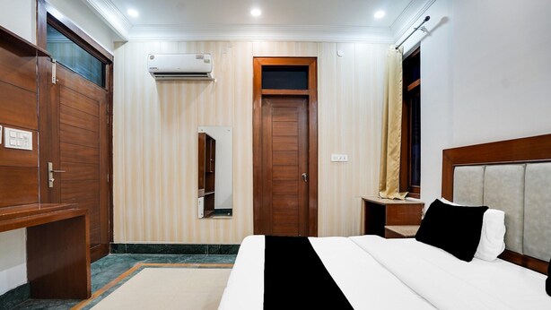 Una habitación de hotel con cama, armario de madera, espejo, equipo de aire acondicionado y ventana con cortinas.