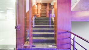 Una escalera con barandilla, una puerta con panel texturizado y una pequeña planta en maceta en el rellano.