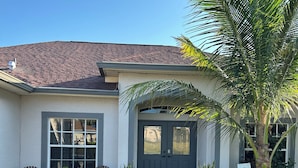 A house with a tiled roof, a front porch with two chairs, a palm tree, and a welcome sign. - Bright 3BR Family Home • 15min to Beach • Quiet, Clean & Comfortable (Fort Myers)