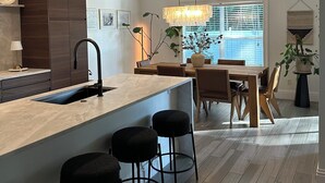 A modern kitchen with a central island, bar stools, a dining table, and a chandelier. - Bright 3BR Family Home • 15min to Beach • Quiet, Clean & Comfortable (Fort Myers)