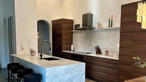 A modern kitchen with a marble island, dark wooden cabinets, and a dining area with a wooden table and bar stools. - Bright 3BR Family Home • 15min to Beach • Quiet, Clean & Comfortable (Fort Myers)