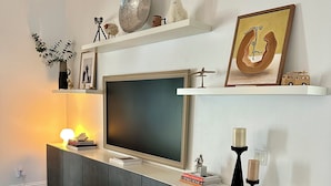 A modern living room with a flat-screen TV, a white console table, decorative items, and a bookshelf. - Bright 3BR Family Home • 15min to Beach • Quiet, Clean & Comfortable (Fort Myers)