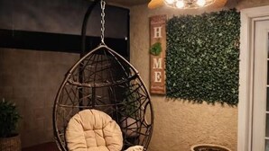 A hanging chair with a cushion, a wall with a green leafy wall, and a sign with the letters 'HME'. - The Cozy Inn (Phoenix)