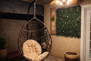 A hanging chair with a cushion, a wall with a green leafy wall, and a sign with the letters 'HME'. - The Cozy Inn (Phoenix)