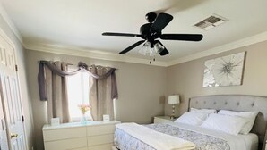 A bedroom with a bed, a ceiling fan, a nightstand, a dresser, and a window with curtains. - The Cozy Inn (Phoenix)