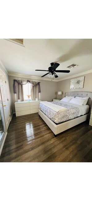 A bedroom with a bed, a ceiling fan, a nightstand, a dresser, and a window with curtains. - The Cozy Inn (Phoenix)