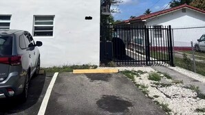 A white building with a red roof, a gated parking area, and a car parked in front.
