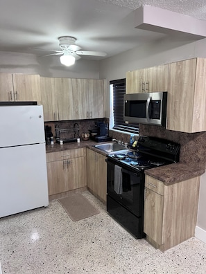 A kitchen with wooden cabinets, a white refrigerator, a microwave, a stove, and a ceiling fan.