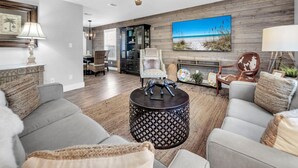 A living room with a fireplace, a ceiling fan, and a large beach painting on the wall. - 1 Almost Heaven (Panama City Beach)