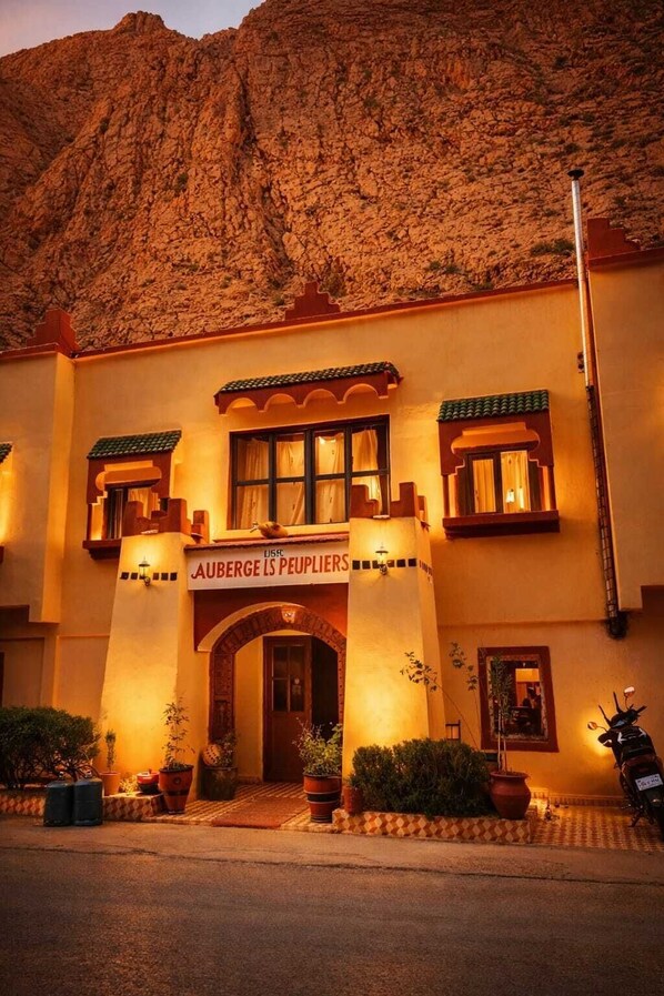 Un hotel con un cartel que dice 'AUBERGE LS PEUPLIERS', que presenta una fachada tradicional con una entrada central, balcones y plantas en macetas.
