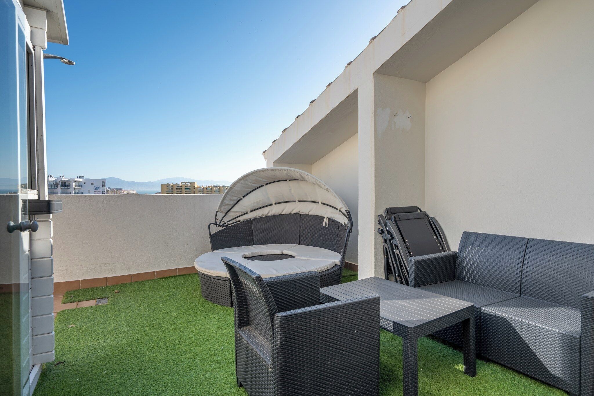 Una terraza en la azotea con un sofá de mimbre, una mesa redonda y una parrilla.