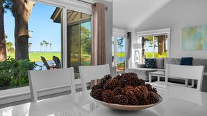 A modern living room with a view of a golf course, a dining table with a pine cone centerpiece, and a cozy seating area. - Fairways 274- Sea Ya Later (Miramar Beach)