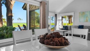A modern living room with a view of a golf course, a dining table with a pine cone centerpiece, and a cozy seating area. - Fairways 274- Sea Ya Later (Miramar Beach)