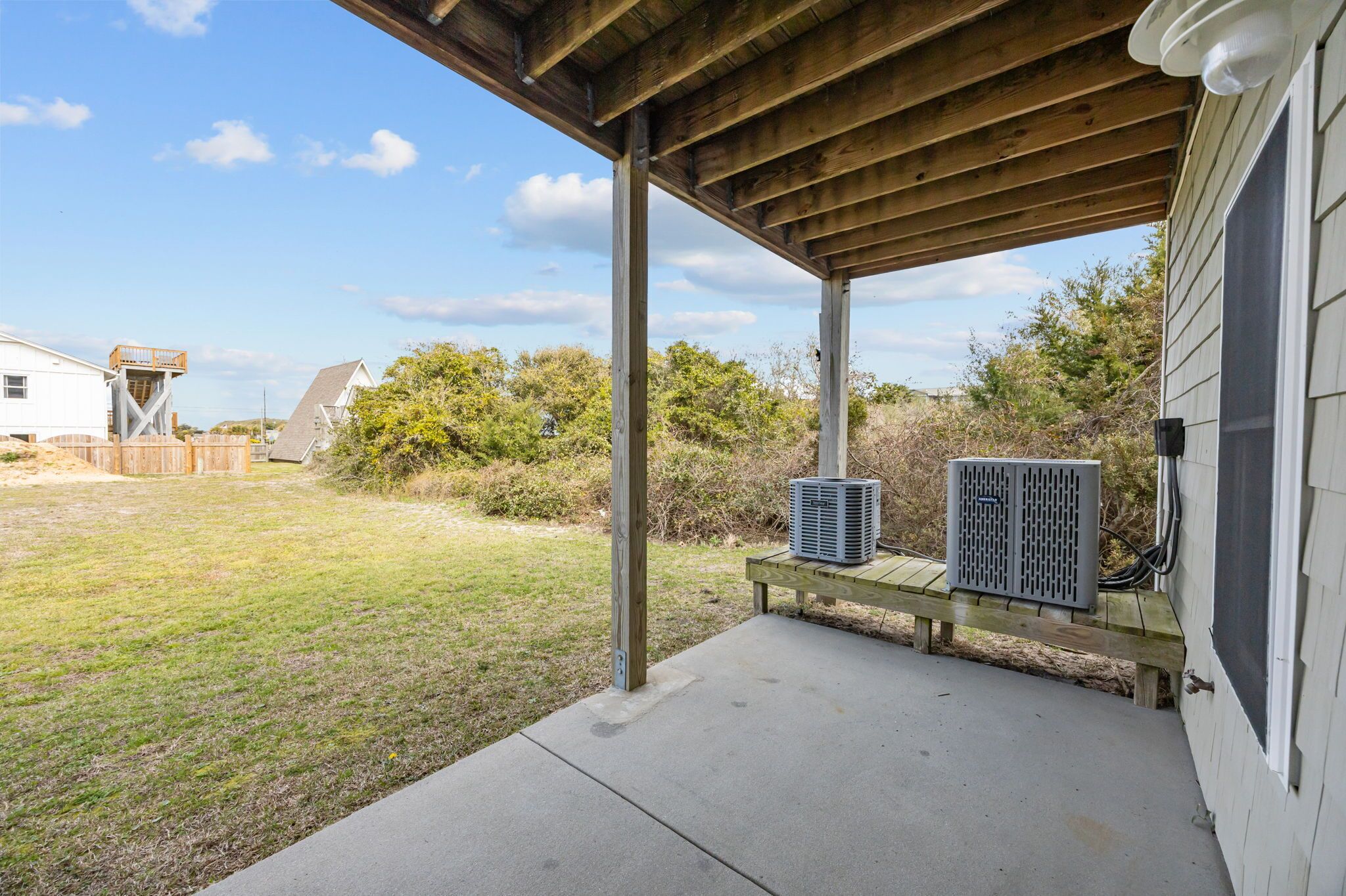 A covered porch with a concrete floor, a wooden bench, and an air conditioning unit.
