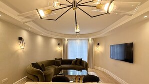 Een moderne woonkamer met een hoekbank, een glazen salontafel en een grote televisie aan de muur.