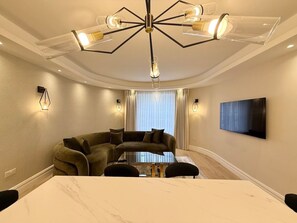 Ein modernes Wohnzimmer mit einem Ecksofa, einem Glastisch und einem großen Fernseher, der an der Wand befestigt ist.