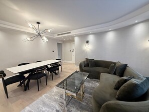 Ein modernes Wohnzimmer mit Essbereich, einem Glastisch, einer Couch und einer Kronleuchter.