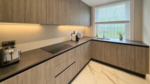 Een moderne keuken met houten kastjes, een ingebouwde toaster, een waterkoker en een raam met zonwering.