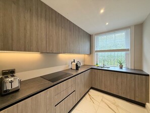Eine moderne Küche mit Holzausstattung, eingebautem Toaster, Wasserkocher und einem Fenster mit Jalousien.