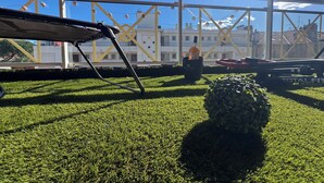 Una terraza en la azotea con césped artificial, una silla, una planta en maceta y una mesa con una botella.