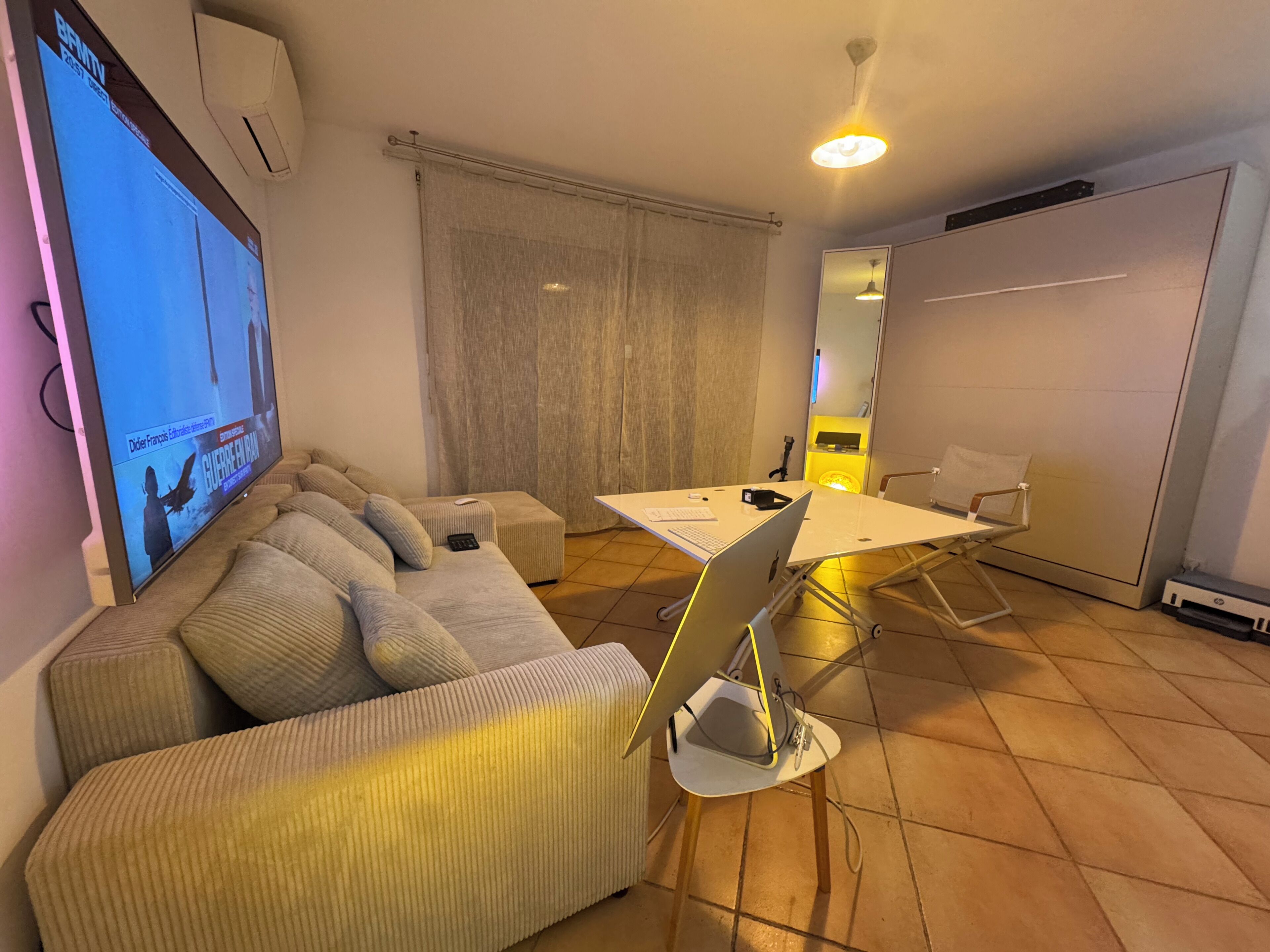 Una sala de estar con un sofá, una mesa de centro, un televisor, un escritorio con una computadora portátil y una silla.