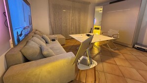 Una sala de estar con un sofá, una mesa de centro, un televisor, un escritorio con una computadora portátil y una silla.