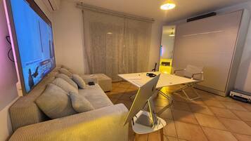 Una sala de estar con un sofá, una mesa de centro, un televisor, un escritorio con una computadora portátil y una silla.