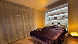 Un dormitorio moderno con cama, una computadora portátil sobre la cama, una lámpara de noche y una cortina.