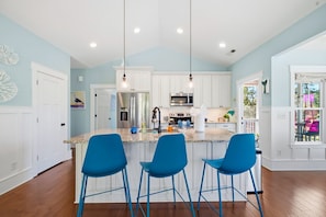 A modern kitchen with white cabinets, a central island with blue bar stools, stainless steel appliances, and pendant lighting. - Private Pool Oasis I Hot Tub I Free Golf Cart! (Oak Island)