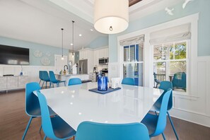 A modern kitchen with white cabinets, blue chairs, and a large white table. - Private Pool Oasis I Hot Tub I Free Golf Cart! (Oak Island)