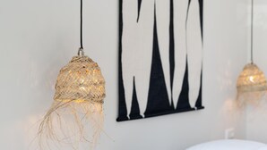 Ein Zimmer mit einem weißen Bett, zwei gewobenen Pendelleuchten und einer abstrakten Wandkunst in Schwarzweiß.