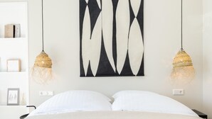 Ein Bett mit weißer Bettwäsche, zwei Pendelleuchten und ein abstraktes Kunstwerk an der Wand.