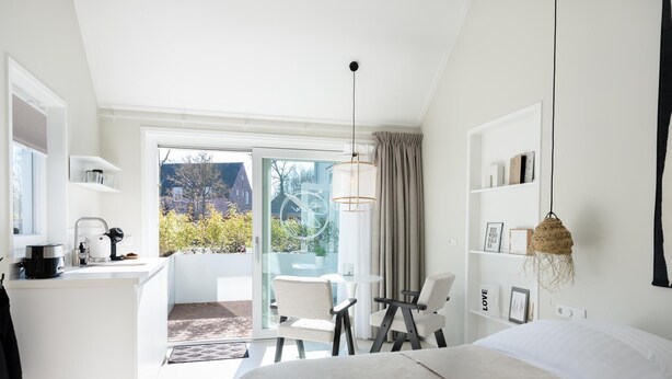 Ein modernes Hotelzimmer mit Bett, Schreibtisch, Stuhl, einem Balkon mit Blick und einer Pendelleuchte.