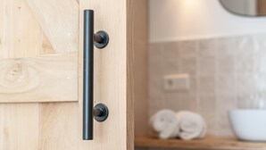 Eine Holztür mit schwarzem Griff, eine Kachelwand und eine weiße Schüssel mit Handtüchern.