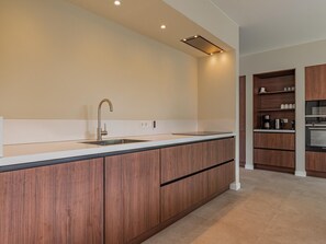 Une cuisine moderne dotée d’un îlot central, de meubles de rangement en bois intégrés, d’un évier en acier inoxydable et d’un four encastré.