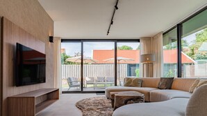 Ein modernes Wohnzimmer mit Flachbildfernseher, Sofa, Couchtisch und großem Fenster.