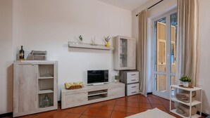 Ein Wohnzimmer mit Fernseher, Holzschränken, einer Glastruhe und einer Schiebetür zum Außenbereich.