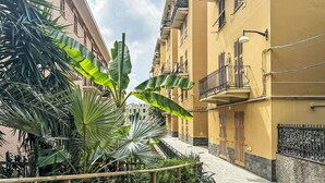 Eine schmale Stadtstraße mit gelben Gebäuden, Balkonen und tropischen Pflanzen.