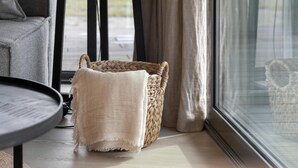 A room with a grey sofa, a woven basket, and a window with curtains. - Delightful holiday home with free view. (Wissenkerke)