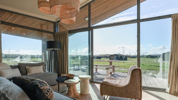 A modern interior with large windows, a sofa, a wicker chair, and a table. - Delightful holiday home with free view. (Wissenkerke)