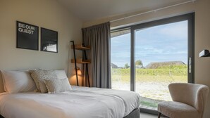 A bedroom with a bed, a chair, a large window, and two wall art pieces. - Delightful holiday home with free view. (Wissenkerke)