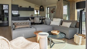 A modern living room with a grey sectional sofa, a round coffee table, and a dining area with a white table and chairs. - Delightful holiday home with free view. (Wissenkerke)