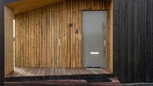 Un bâtiment moderne doté d’une façade en bois, d’une porte grise et d’un petit espace extérieur avec un banc.