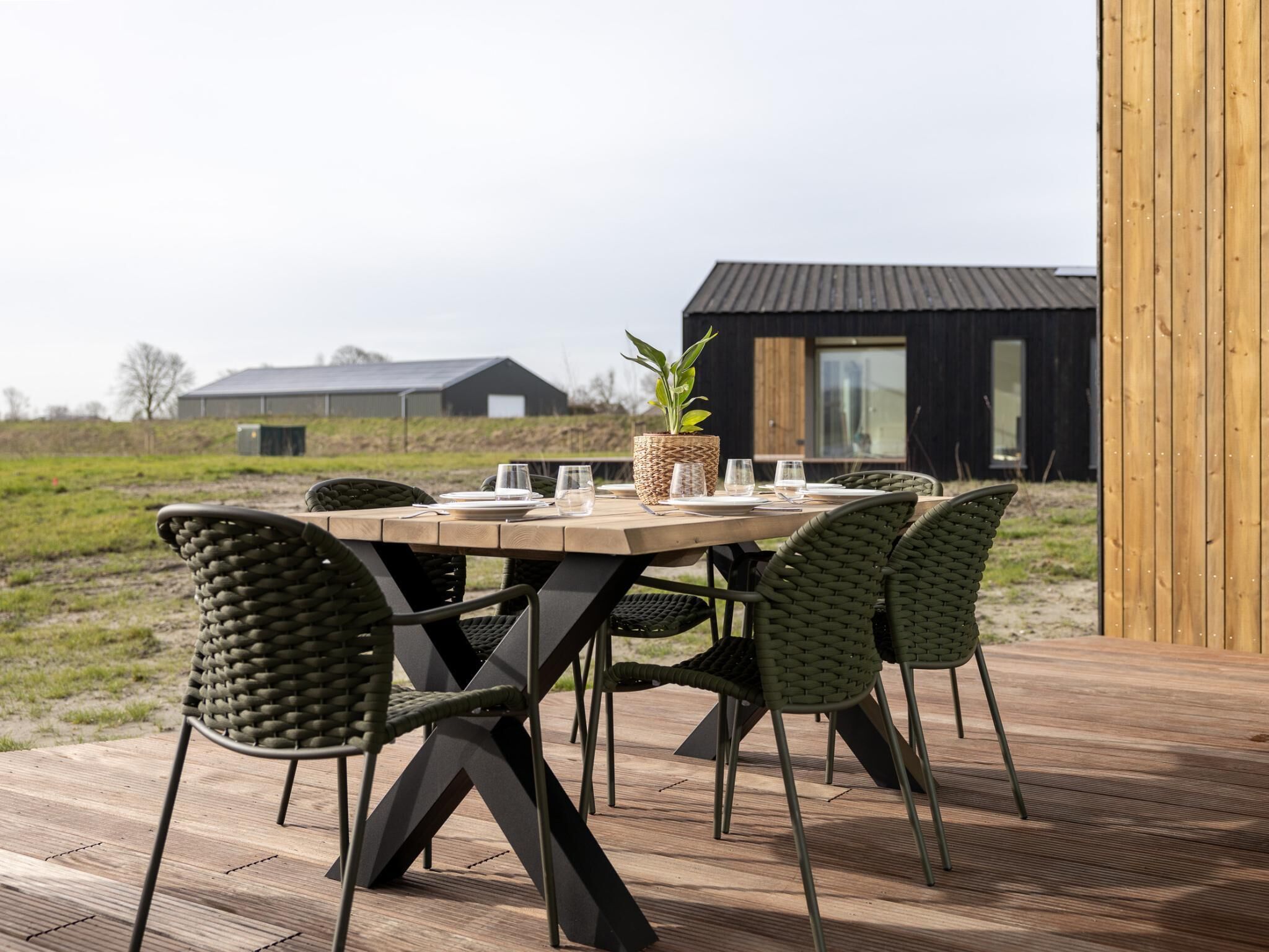 Ein runder Holztisch mit Stühlen, einem Blumentopf und Gläsern auf einer Terrasse.