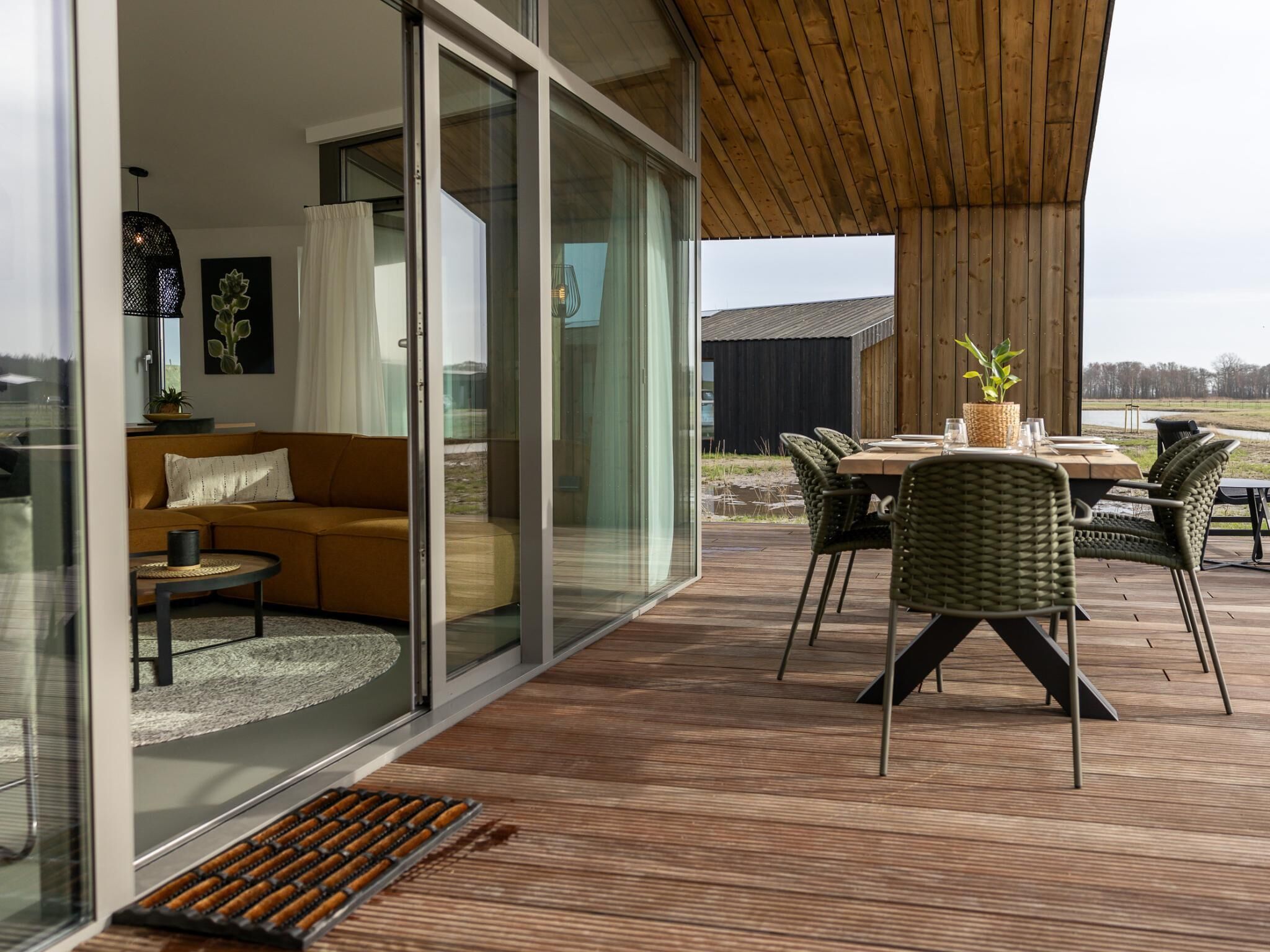 Uma sala de estar moderna com porta de vidro que dá para um deck externo, teto de madeira e vista para o exterior.