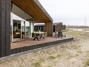 Un edificio moderno con terraza de madera, mobiliario exterior y vistas del paisaje circundante.