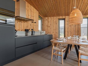 Eine moderne Küche mit Holzvertäfelung, einem Esstisch für vier Personen und einer großen, gewebten Pendelleuchte.
